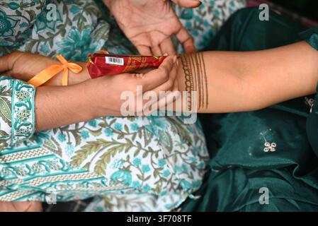 Prima di una mano di artista che applica un disegno di hennè mehndi sul braccio di una giovane donna usando un cono rosso durante la cerimonia mehndi di un matrimonio indiano Foto Stock