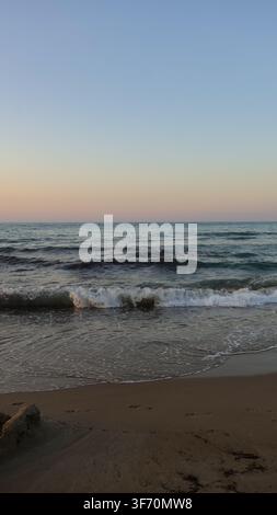 Vista verticale di un'onda oceanica che si infrange sulla spiaggia al crepuscolo con colori smorzati e atmosfera malinconica a Creta, Grecia. Foto Stock