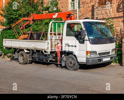 Camion bianco con gru arancione parcheggiato in strada. Il cassone del camion trasporta tronchi e attrezzature Foto Stock