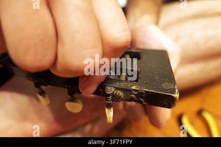 Mano che cura con attenzione una vecchia chitarra acustica, concentrandosi sul meccanismo intricato dei piroli e del capotasto, riflettendo l'artigianalità e Foto Stock