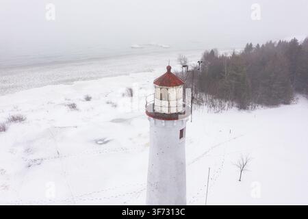 Veduta aerea del faro di Sturgeon Point circondato da terreno coperto di neve e riva ghiacciata ad Harrisville, Michigan, Stati Uniti. Foto Stock
