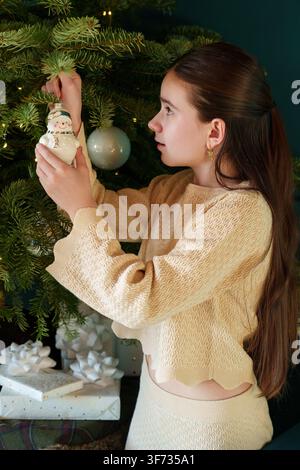 Ragazza adolescente che decora l'albero di Natale con un'ornament a casa Foto Stock