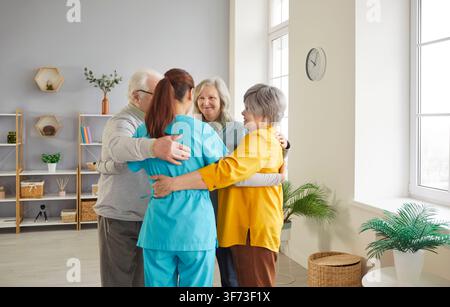 Anziani che abbracciano una giovane infermiera, condividendo un momento caldo di cura e sostegno in una struttura medica. Foto Stock