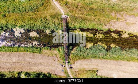 Vista aerea dall'alto di un ponte di legno stretto su un ruscello con un gruppo di persone che lo attraversa Foto Stock