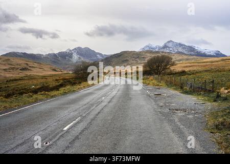 Strada rurale in inverno si avvicina alle montagne del Parco Nazionale di Eryri Snowdonia Foto Stock