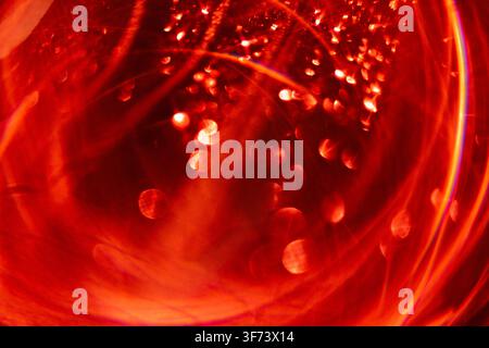Vista ravvicinata di liquido rosso con bolle e riflessi di luce, che crea un effetto visivo astratto e vibrante all'interno di un contenitore di vetro trasparente Foto Stock