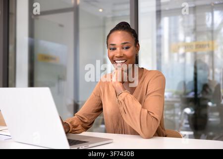 Donna professionista africana seduta alla scrivania dell'ufficio con laptop Foto Stock