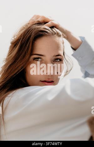 Ritratto di donna viso bella giovane donna che posa con la mano tra i capelli su sfondo luminoso per un concetto di stile di vita e bellezza Foto Stock