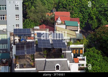 Quartiere urbano vietnamita con pannelli solari fotovoltaici installati sui tetti, circondato da alberi fitti, edifici residenziali e sostenibili Foto Stock