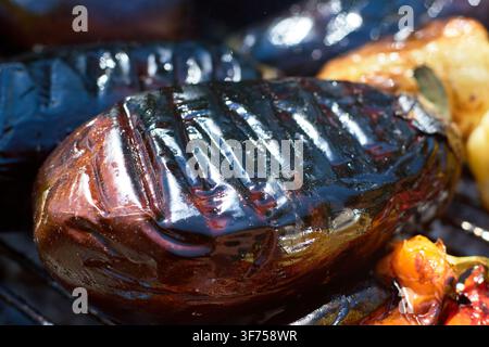 Prima vista di melanzana fresca grigliata su un barbecue caldo con segni di grigliatura distinti e superficie lucida. Foto Stock