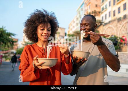 Diversi giovani amici che si godono il cibo di strada insieme, condividendo un momento multiculturale felice e autentico Foto Stock
