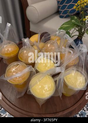 Diversi frullati di frutta gialli in bicchieri di plastica da asporto con cannucce. Diversi succhi tropicali rinfrescanti confezionati in contenitori monouso con coperchio a cupola Foto Stock