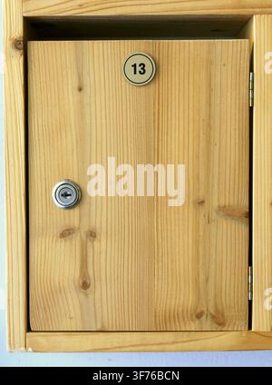 Porta dell'armadietto in legno con un'etichetta circolare numero 13 e una serratura a camme argentata, che offre un deposito sicuro o funge da scomparto per la cassetta delle lettere personale in Foto Stock
