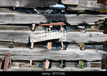 Muro di legno antico carbonizzato e segnato dal tempo di un edificio bruciato con cardini di ferro arrugginiti e fori di bruciatura Foto Stock