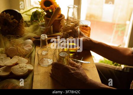Mani che versano olio d'oliva in un bicchiere piccolo su un tavolo di legno con pane Foto Stock