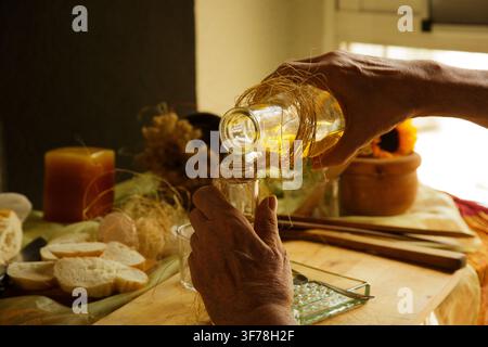 Mani che versano olio d'oliva dorato da una bottiglia più grande a una più piccola Foto Stock