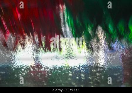 Autolavaggio, foto astratta con sfocatura di movimento, messa a fuoco sull'acqua sul parabrezza, concetto di sfondo per servizi di pulizia e trasporto, spazio per il testo Foto Stock