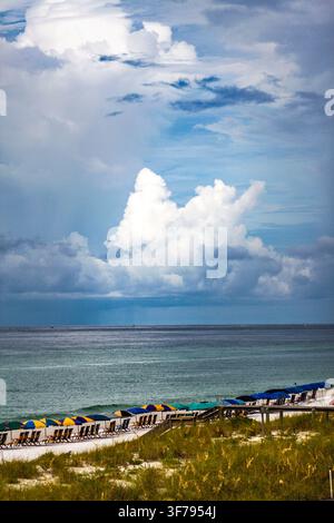 Nuvole tempestose si addensano sopra la spiaggia di Destin, in Florida. Sedie e ombrelloni vuoti costeggiano la riva, incorniciati da una duna erbosa in primo piano. Foto Stock