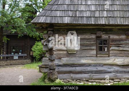 Vista esterna di una vecchia casa tradizionale in tronchi con pareti di legno intrecciate, un tetto di scandole, una piccola finestra e un manufatto in legno intagliato Foto Stock