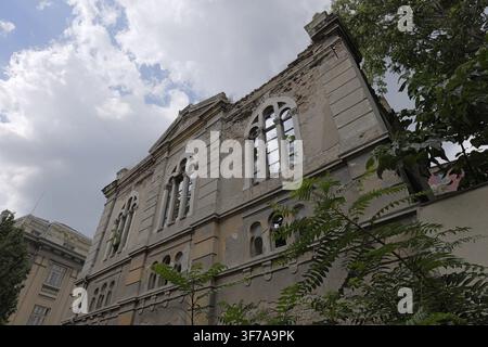 Facciata di un edificio sinagogale storico in rovina a Varna. Rovine di una sinagoga sefardita abbandonata sotto un cielo nuvoloso. Ripresa ad angolo basso di un antico edificio in mattoni. Foto Stock