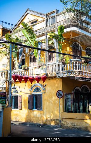 Edificio coloniale tradizionale giallo con lanterne rosse appese sopra la strada a Hoi An, Vietnam Foto Stock