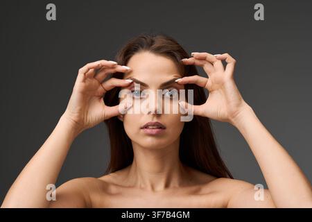 Concetto di blefaroplastica e correzione delle palpebre. Ritratto in primo piano di una donna che mostra le condizioni delle sue palpebre superiori e inferiori toccando la s Foto Stock