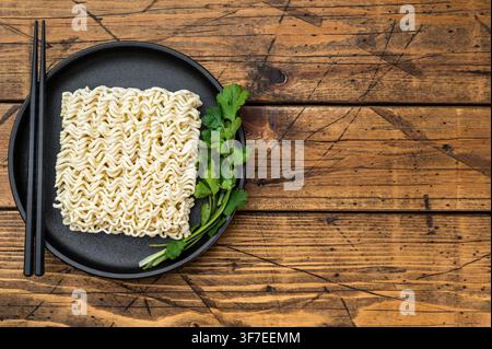 Mattonella di noodles istantanei di grano crudo con coriandolo su piatto nero sopra superficie in legno vintage concetto minimo di cibo pronto asiatico Foto Stock