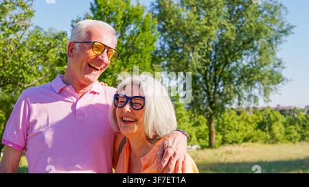 Coppia di anziani felici che si abbracciano e ridono in un parco soleggiato Foto Stock