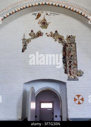 un arco dipinto e una cornice a affresco decorativa su un muro di mattoni imbiancato a calce incorniciano la porta all'interno della chiesa di Ebeltoft in Danimarca Foto Stock