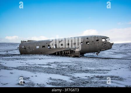 Il lato arrugginito del famoso relitto dell'aereo Douglas DC-3 poggia sull'ampia distesa desolata di sabbia vulcanica nera mescolata a neve a Sólheimasandur, Islanda Foto Stock
