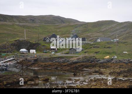 Costiera di Skarsvåg con riva ricoperta di alghe e edifici grigi sullo sfondo in una giornata estiva nuvolosa. Foto Stock