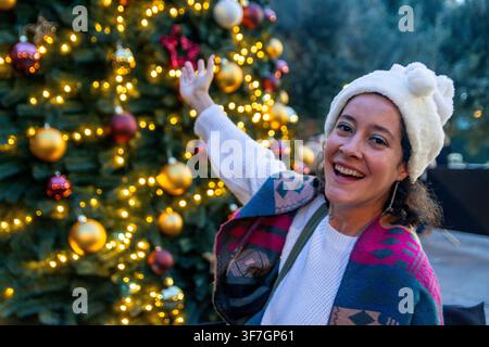 Donna allegra che celebra la stagione delle festività vicino a un albero di Natale illuminato Foto Stock