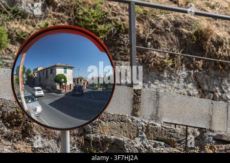 Specchio di sicurezza panoramico stradale su una curva stretta con edifici antichi sullo sfondo. Controllo del traffico, sicurezza urbana e concetto di veduta stradale. Foto Stock