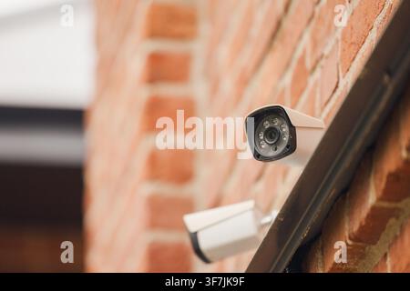 Telecamere di sicurezza montate su un muro di mattoni rossi che monitorano un'area pubblica urbana Foto Stock