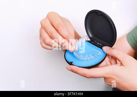 Prima di mani femminili che presentano allineatori dentali trasparenti in una custodia protettiva aperta su uno sfondo bianco pulito con spazio per il testo. Foto Stock