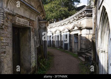 Un sentiero stretto si snoda tra le tombe di pietra erodate del cimitero di Highgate. Famoso cimitero vittoriano a Londra, UK, con architettura gotica. Foto Stock