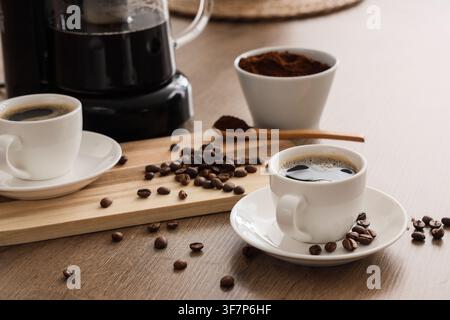 Caffè appena preparato in tazze bianche con chicchi tostati e caffè macinato su un tavolo di legno, bevanda mattutina Foto Stock