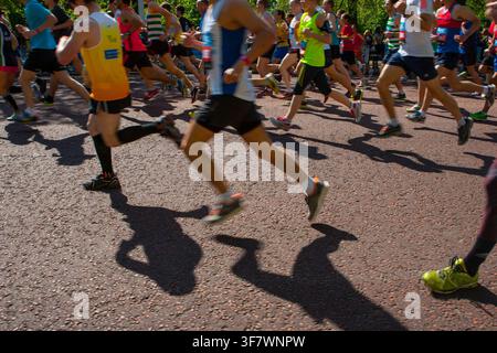 Una vista ravvicinata delle gambe e delle ombre dei corridori in movimento durante la Bupa London 10.000, corsa su strada nel centro di Londra il 27 maggio 2013. Foto Stock