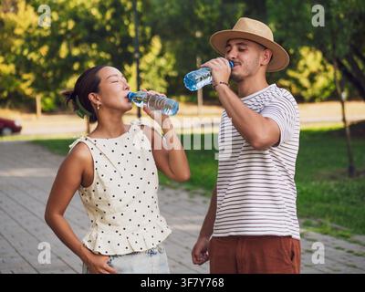 Una giovane coppia beve acqua nel parco in una giornata d'estate soleggiata. Foto Stock