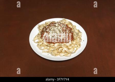 Tagliatelle condite con salsa bolognese, formaggio grattugiato ed erbe, disposte su uno sfondo marrone scuro. Foto Stock
