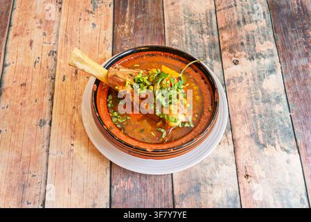 Stinco d'agnello brasato con piselli, carote e coriandolo, servito in una ciotola tradizionale in argilla (tagine) Foto Stock