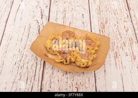 Dumplings siumai fritti disposti in una barchetta da asporto in carta kraft su un tavolo di legno rustico. Foto Stock