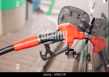 Ugello di rifornimento rosso inserito nel serbatoio della benzina di un'auto alla stazione di servizio in primo piano, concetto di rifornimento di carburante e economia dei trasporti. Foto di alta qualità Foto Stock