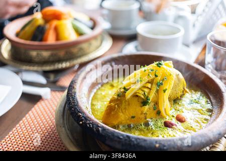 Godersi il tajine marocchino tradizionale e il couscous serviti in un ambiente vivace con verdure colorate ed erbe aromatiche Foto Stock