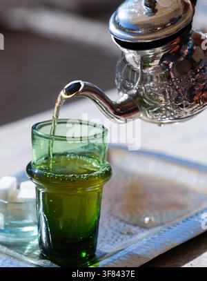 Tè alla menta tradizionale servito in una teiera d'argento con zollette di zucchero su un vassoio di metallo in un'ambientazione marocchina Foto Stock