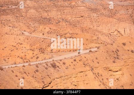 Ciclista che pedala su una strada sterrata attraverso le badland del deserto di Gorafe a Granada, Spagna, con formazioni erosionali e paesaggio desertico Foto Stock