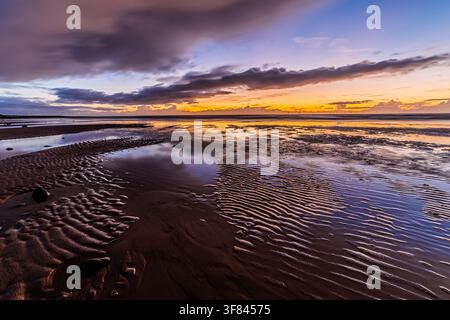 Vista del Mar d'Irlanda da Walney Island con un tramonto sulla costa della Cumbria e modelli di marea in primo piano Foto Stock