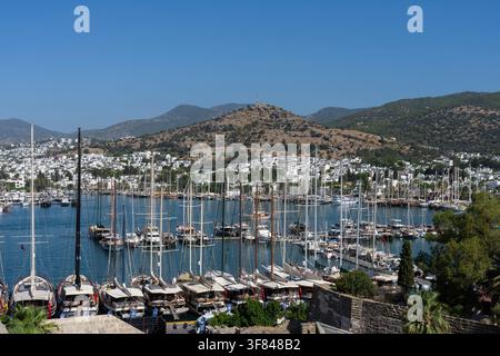 Bella vista del porto di Bodrum con barche e colline sotto un cielo blu limpido al sole del pomeriggio Foto Stock