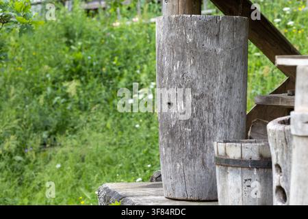 Un tronco d'albero cavo tradizionale funge da alveare in legno. L'oggetto si trova all'aperto su un gradino di legno vicino a secchi di legno, su uno sfondo sfocato Foto Stock