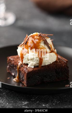 Delizioso brownie servito con gelato e guarnizione al caramello su tavolo nero, primo piano Foto Stock